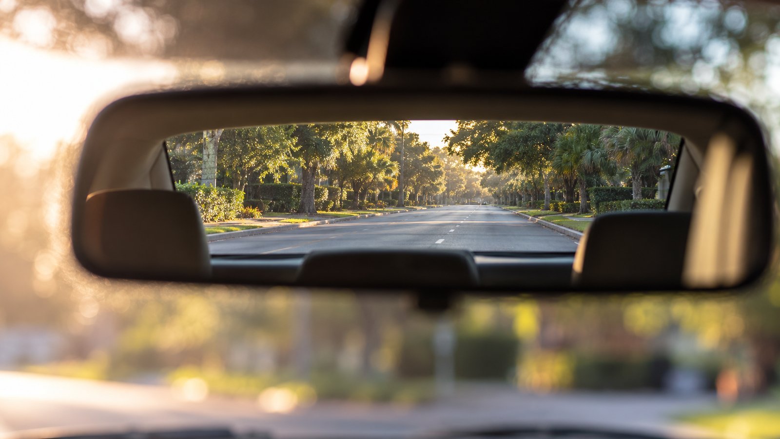 View through a car's rear-view mirror down a quiet road - Uninsured and Underinsured Motorist Coverage